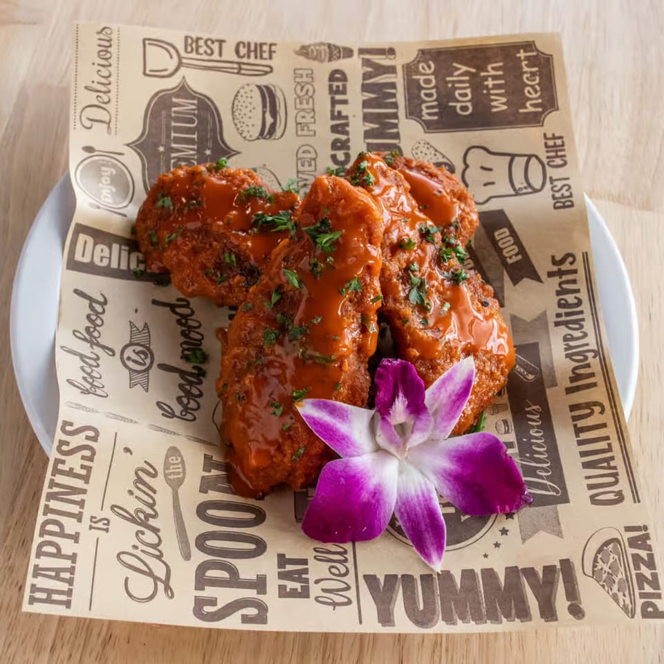 Maggy's House chicken wings, drizzled with red sauce and parsley, on branded paper with a purple orchid.