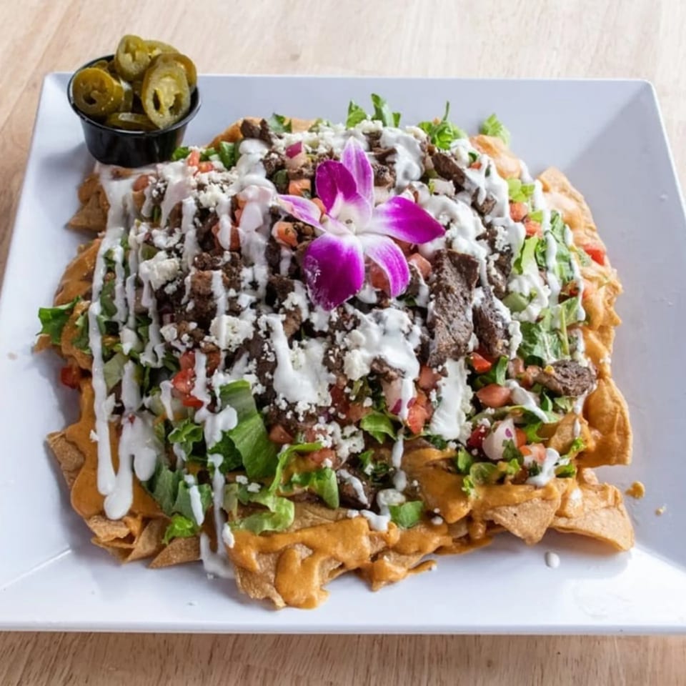 Maggy's House nachos with steak, cheese, lettuce, tomatoes, and a purple orchid garnish.